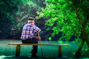 elderly man meditating on bench near lake